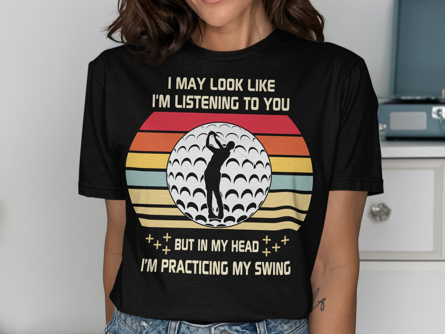 Black t-shirt with golf ball and text: "I MAY LOOK LIKE I'M LISTENING TO YOU BUT IN MY HEAD I'M PRACTICING MY SWING."