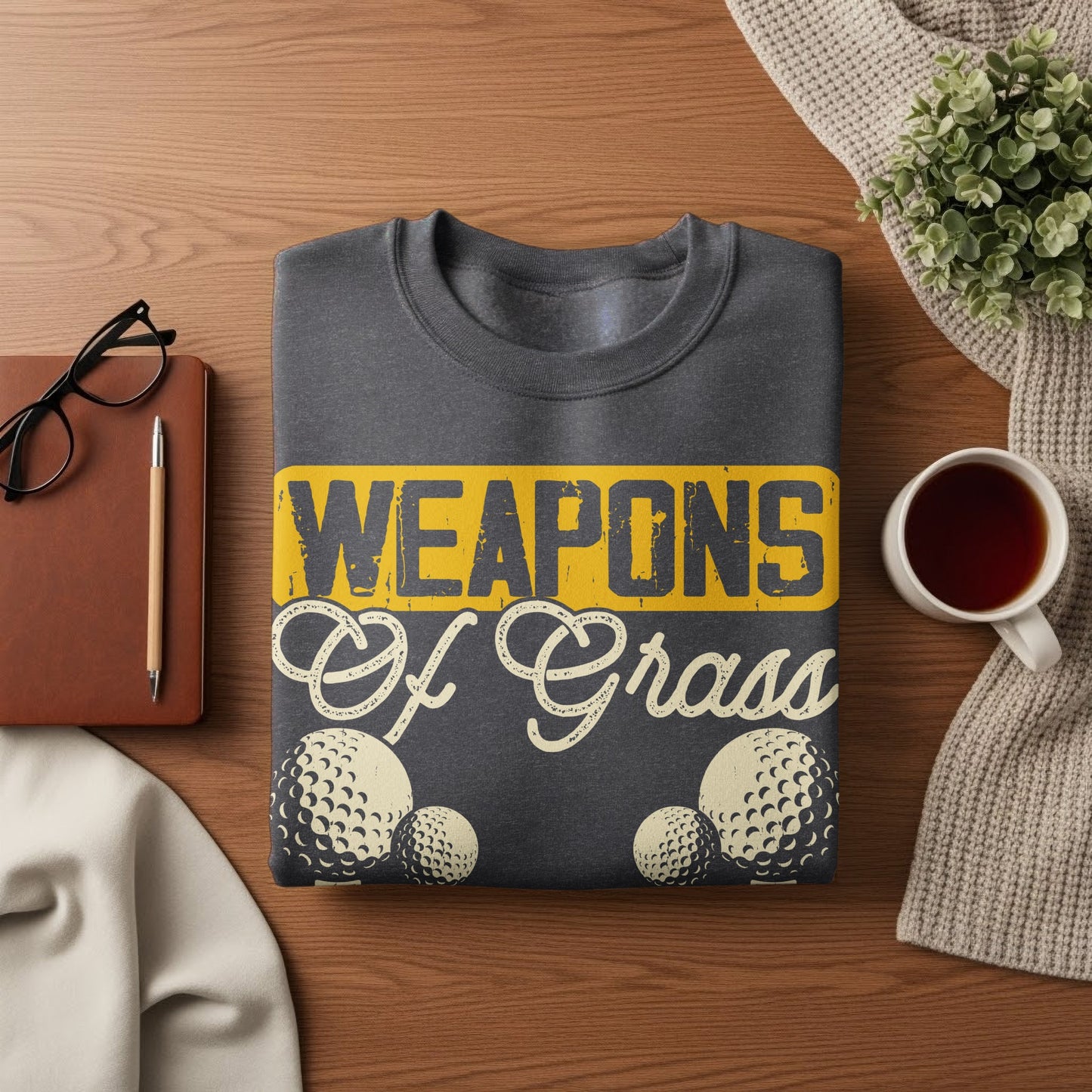 Dark gray sweatshirt with "WEAPONS Of Grass" text and golf ball graphics.