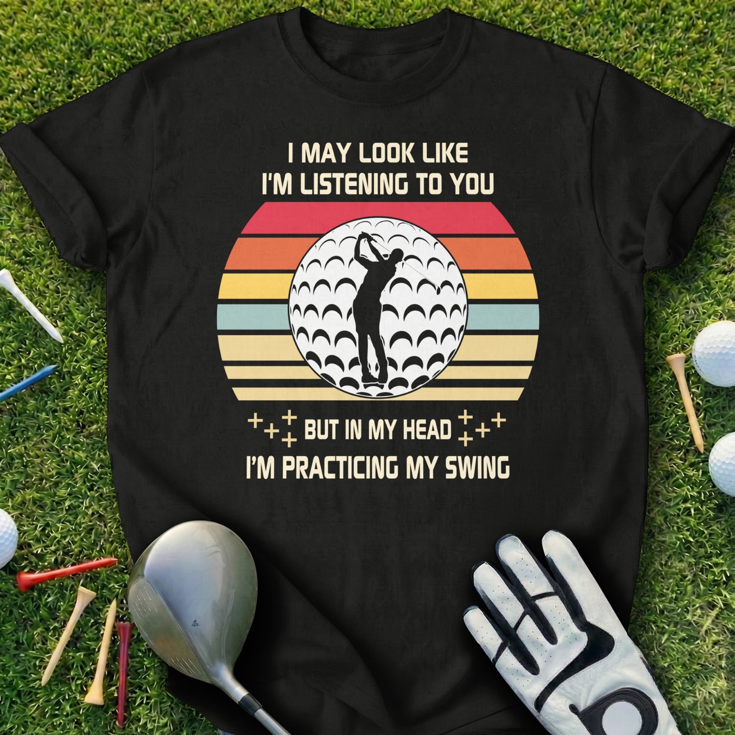 Black t-shirt with golf ball and text: "I MAY LOOK LIKE I'M LISTENING TO YOU BUT IN MY HEAD I'M PRACTICING MY SWING."