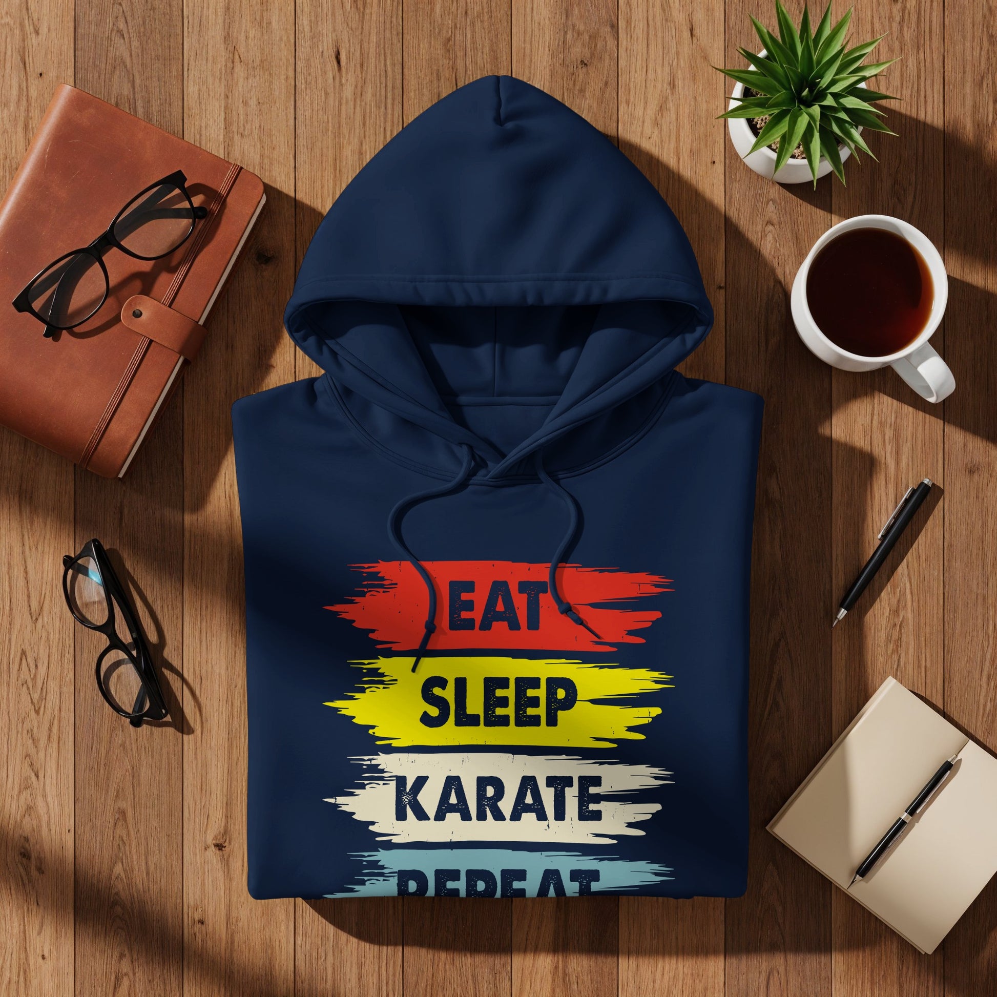 Navy hoodie with "EAT SLEEP KARATE REPEAT" text graphic on a wooden table.