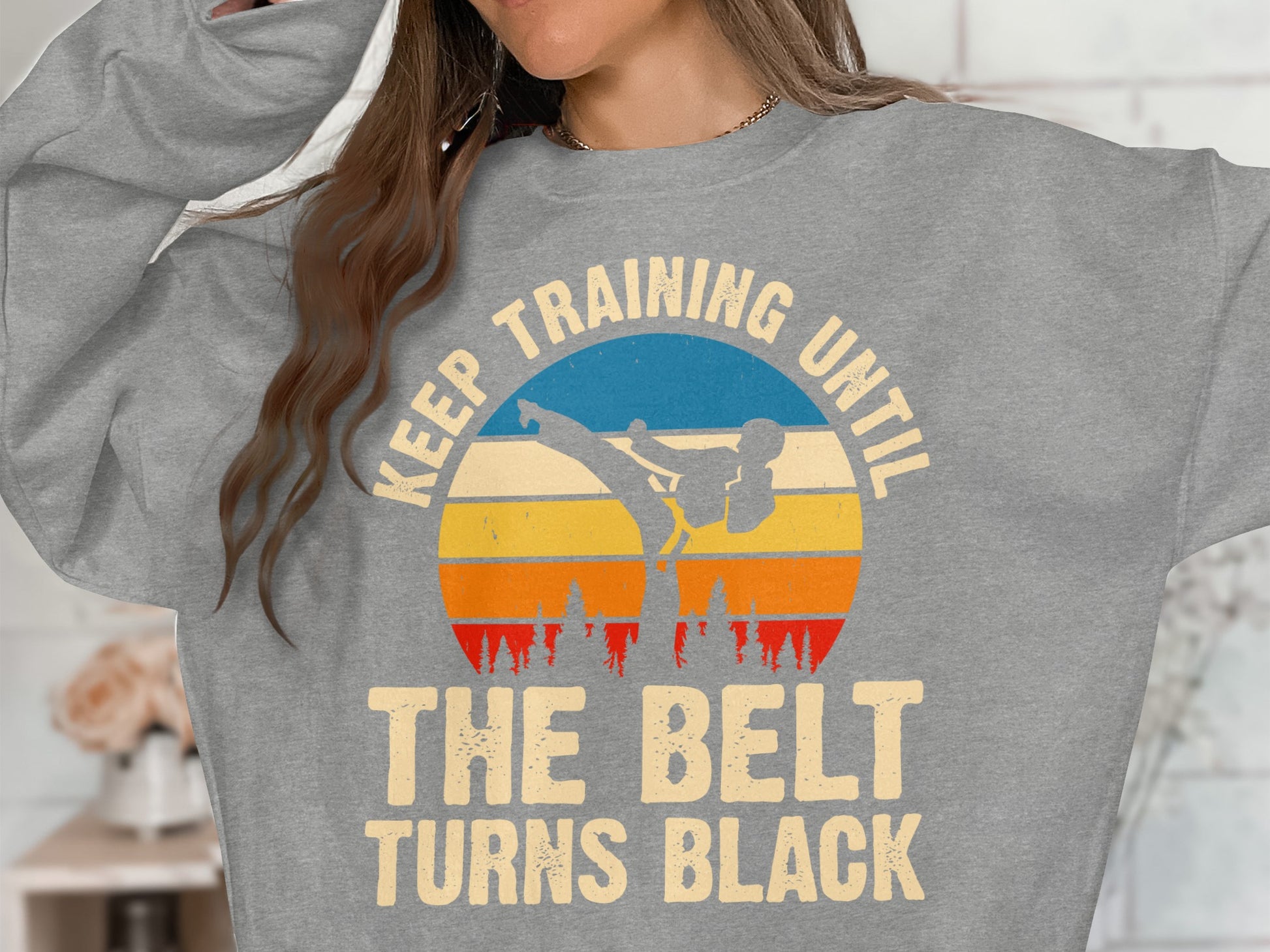 Grey sweatshirt with sunset, martial artist silhouette, and text "KEEP TRAINING UNTIL THE BELT TURNS BLACK".