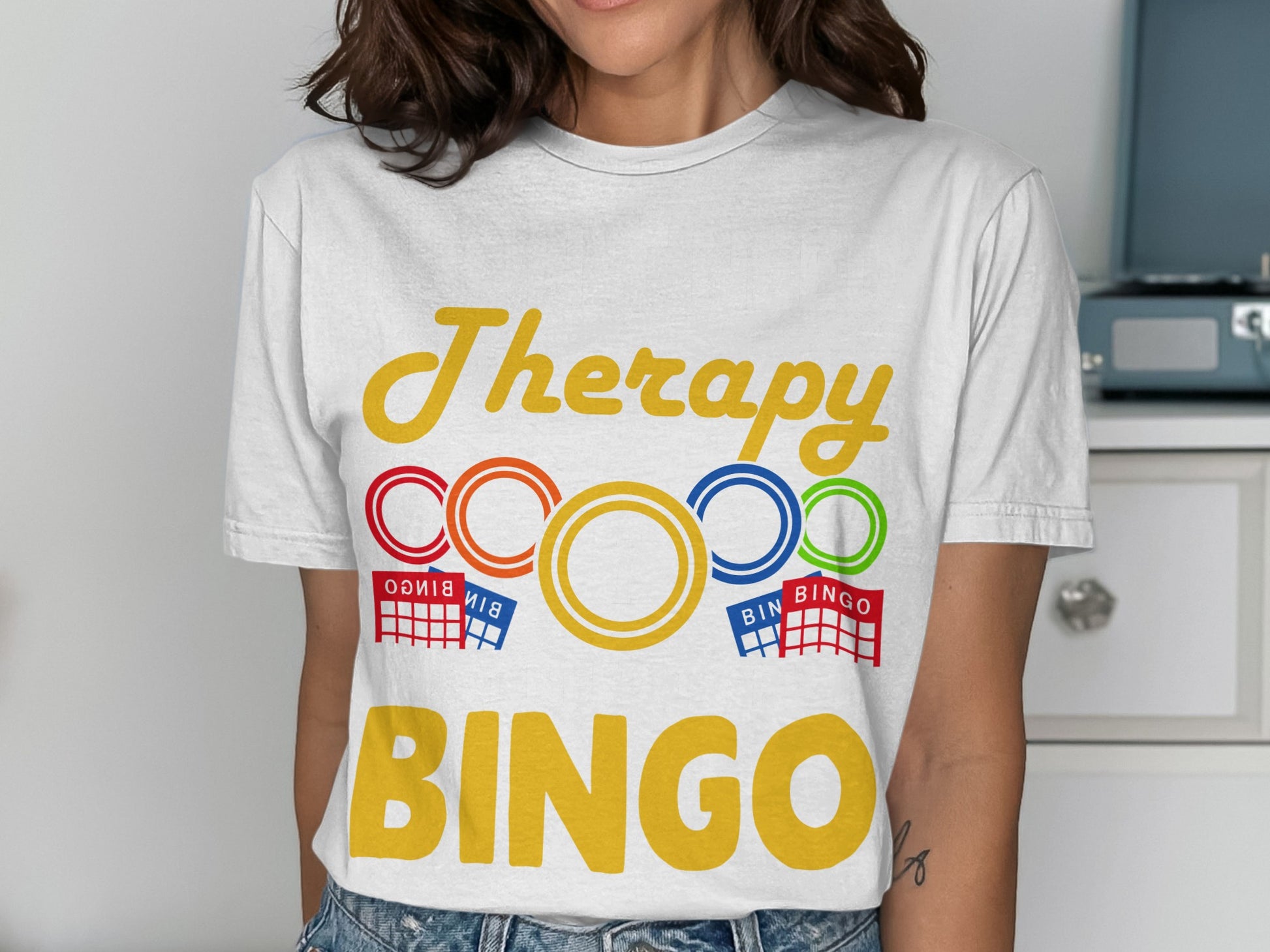 White t-shirt with "Therapy" and "BINGO" in colorful text, with bingo card graphics.