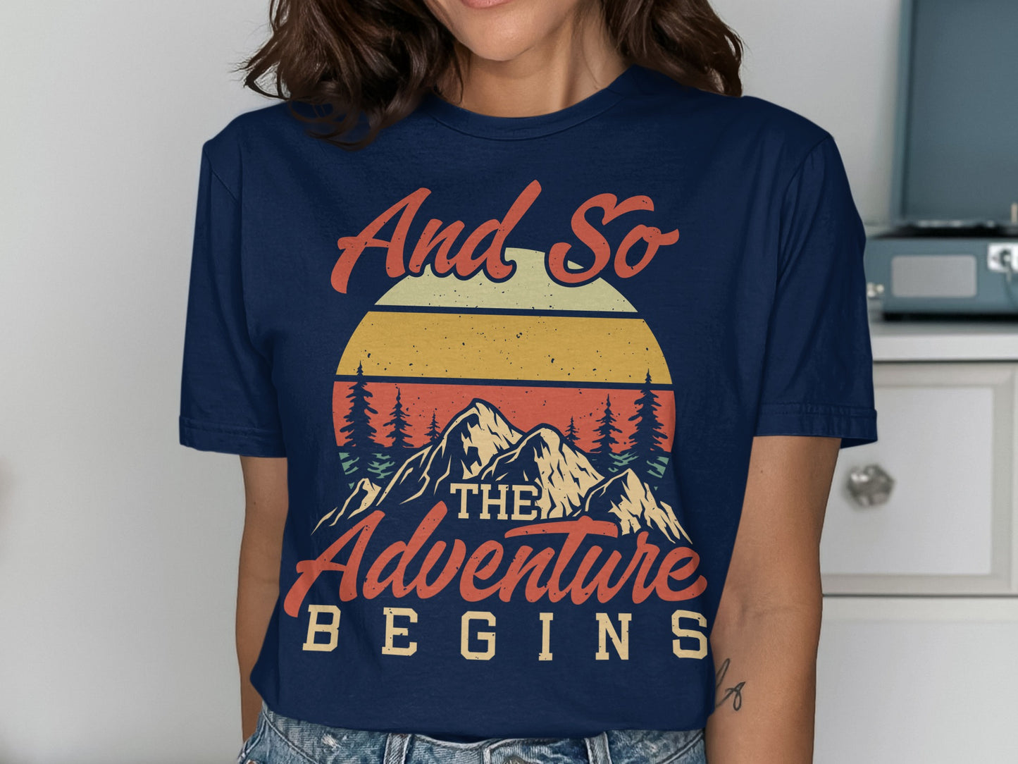 Navy t-shirt with "And so the adventure begins" mountain sunset graphic.