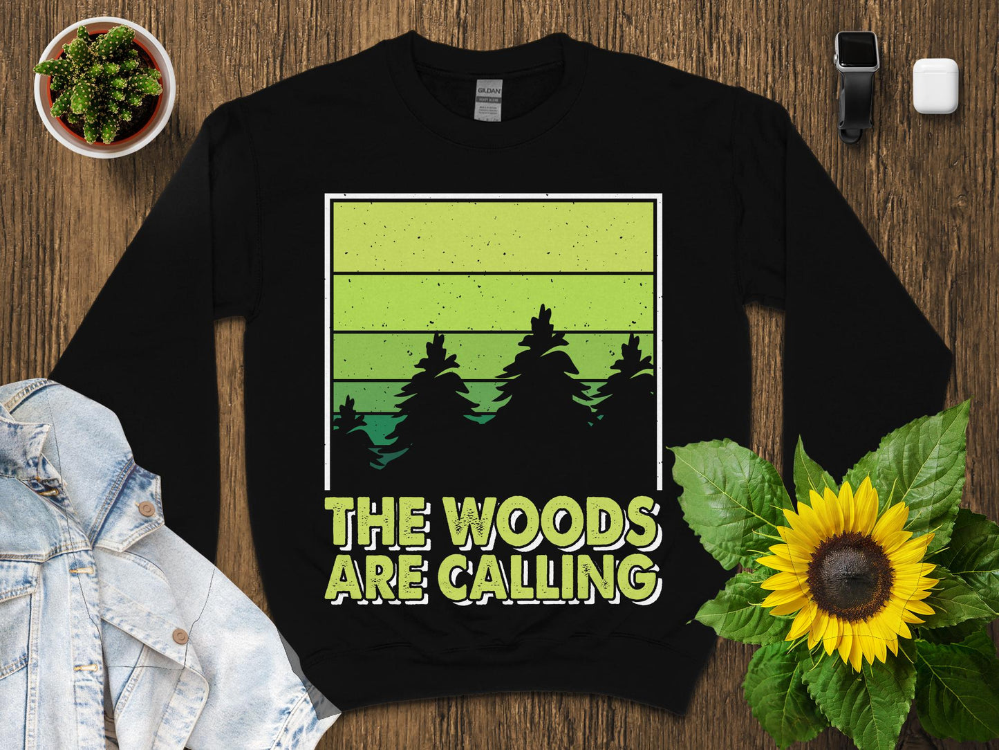 Black sweatshirt with "The Woods Are Calling" text and green gradient forest scene.