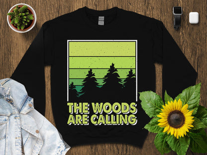 Black sweatshirt with "The Woods Are Calling" text and green gradient forest scene.