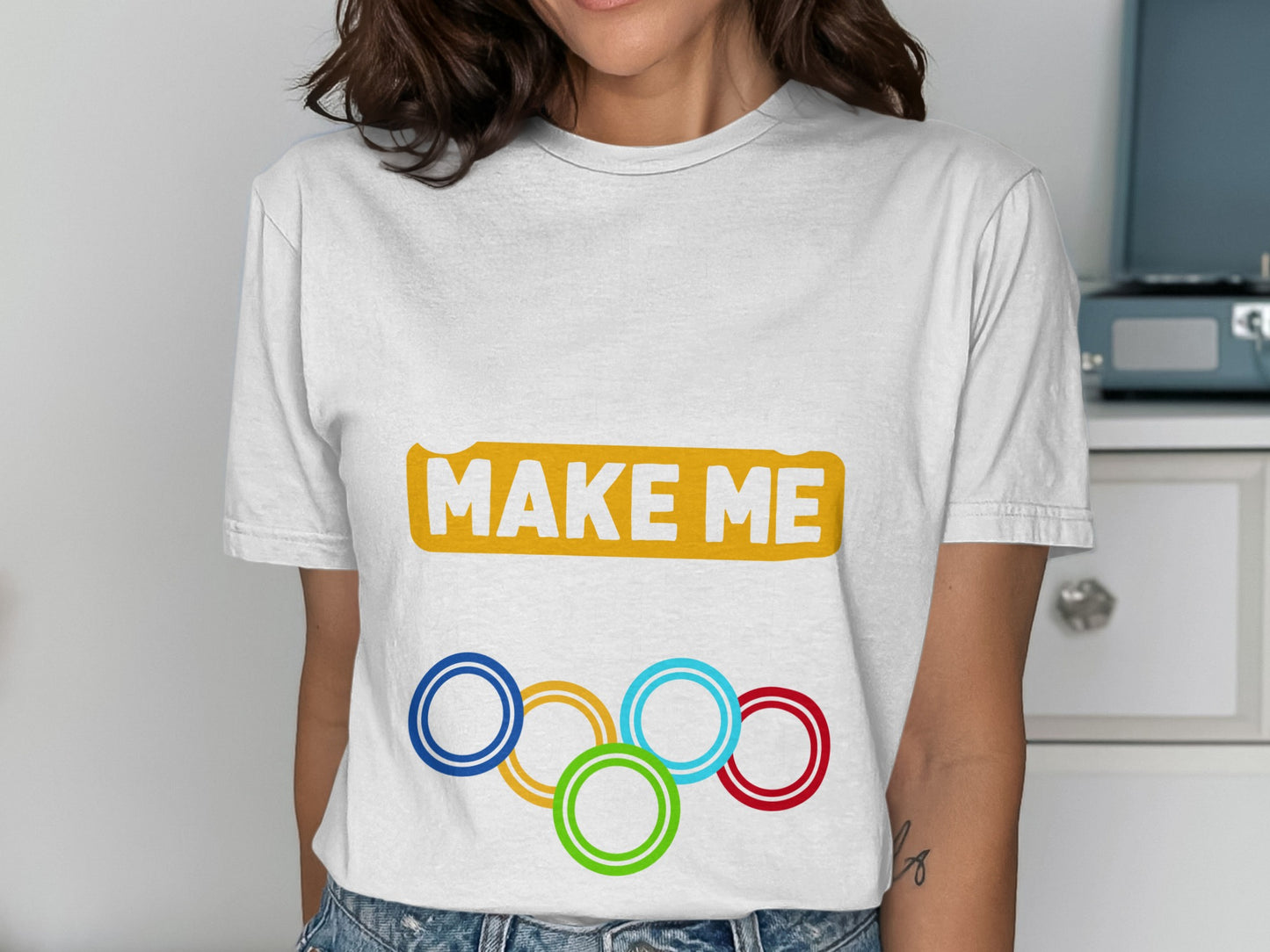White t-shirt with "MAKE ME" and Olympic rings logo.